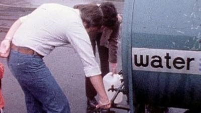 Man fills bucket from water bowser 1976