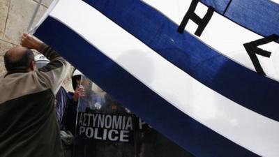 An anti-austerity protester waves a Greek flag in front of the heavily guarded parliament in Athens