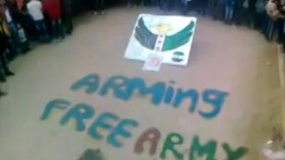 Crowd stand around words saying 'ARMING FREE ARMY'