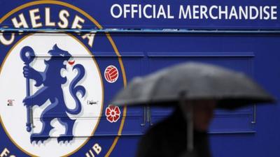 A man carrying an umbrella passes an closed merchandise kiosk at Chelsea football club.