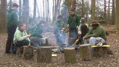 Children sitting around a campfire toasting sausages