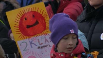 Child wearing woolly hat stands in front of child's poster showing the sun.