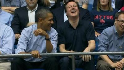 Barack Obama and David Cameron share a joke while watching the basketball game.