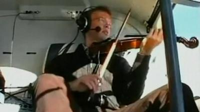 A man plays a violin on board a helicopter.