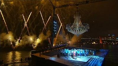 Fireworks are launched around a floodlit opera staged at night on a massive open air barge.