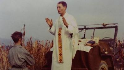 Father Emil Kapaun prays over a soldier during the Korean War