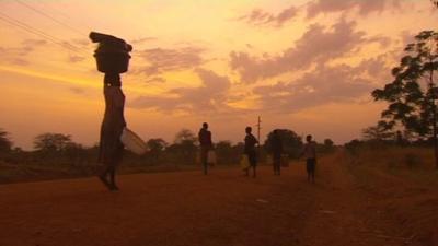 A woman carries a load above her head as the sun rises.