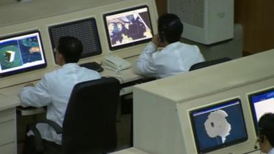 Men looking at computers inside North Korea's mission control