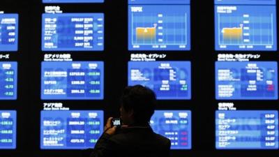 Man in front of Tokyo Stock Exchange displays showing market prices