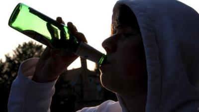 Teenage boy swigging from beer bottle