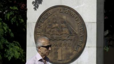 Man makes his way past a replica of a one drachma coin outside the Athens Town Hall