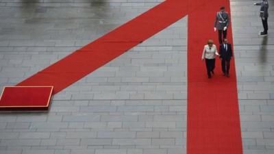 German Chancellor Angela Merkel (L) and the new French president Francois Hollande walk to review a guard of honour in front of the German Chancellery