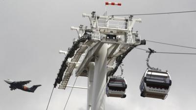 Cable cars suspended on wires with aeroplane flying in the distance