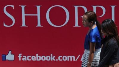 Thai women walk past a Facebook logo displayed at shopping mall in Bangkok