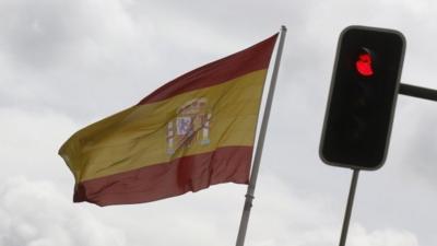 A Spanish national flag flies near a red traffic light in central Madrid