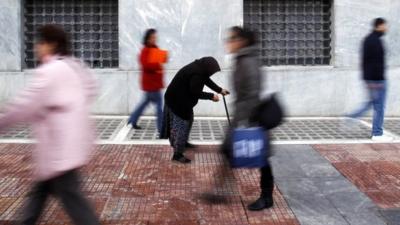 A woman begs as shoppers walk by in central Athens