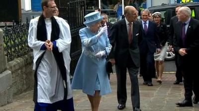 The Queen and Prince Philip waving to crowds with church minister beside them