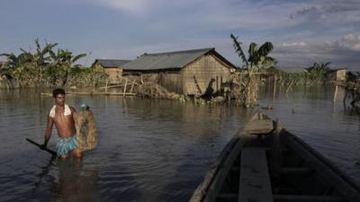 An Indian villager wades through flood waters at Gagalmari village in Assam state