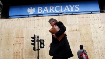 Pedestrians walking past a Barclays bank logo in central London