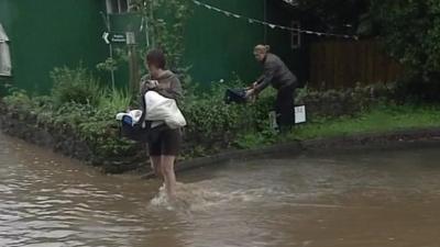 Woman carries baby across flood water