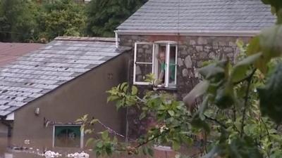 Couple look out of their home's top floor window at flood below