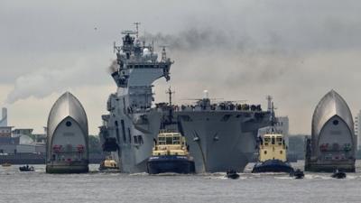 HMS Ocean sails through the Thames Barrier on the River Thames to dock at Greenwich, London