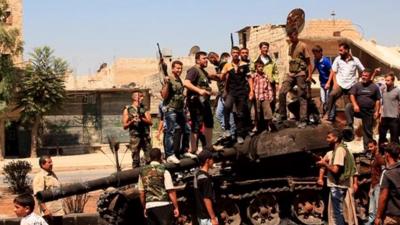 Rebel fighters stand on top of a government tank in Aleppo