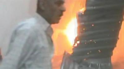 Buildings on fire as man walks past in southern Damascus