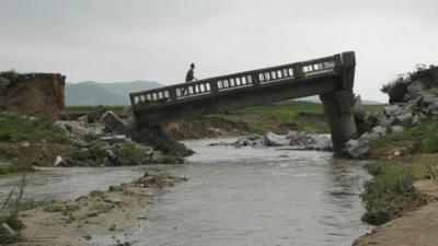 A man walks over a damaged bridge after heavy rain in Onchon County, North Korea