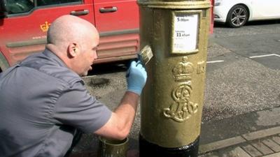 Man paints a post box gold