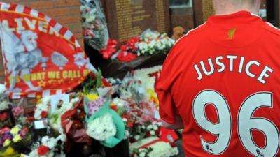 Floral tributes and man wearing 'Justice 96' shirt