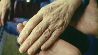 Elderly person holding hands with a carer