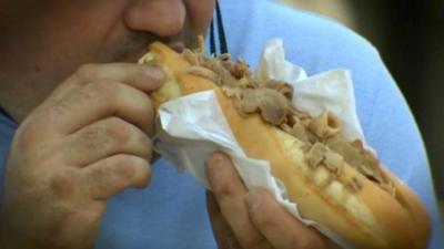 Large man eating a meat roll