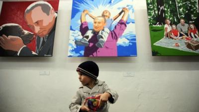 Small boy in front of Putin paintings