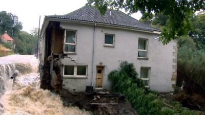 House with a wall missing surrounded by flood water