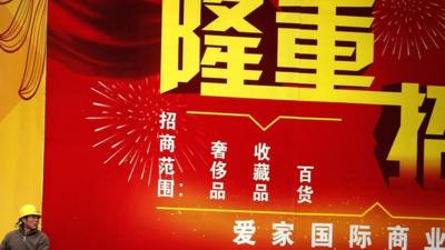 A construction worker smokes a cigarette in front of a billboard advertising investment opportunities in Beijing