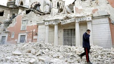Italian military carabinieri walks on debris past destroyed buildings after an earthquake