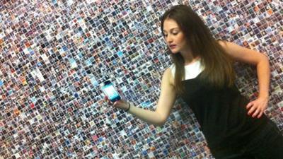 Employee of Mashable holding a mobile phone in front of faces on a wall