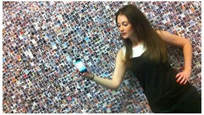 Employee of Mashable holding a mobile phone in front of faces on a wall