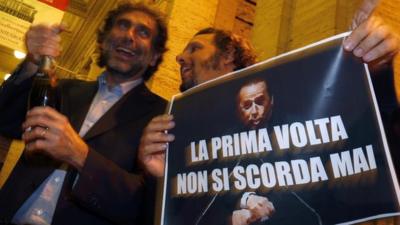 People hold a picture of Italy"s former PM Berlusconi with words that read "You Never Forget Your First Time" as they celebrate after Berlusconi was sentenced to jail for tax fraud in downtown Rome