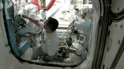 Station commander Sunita Williams and flight engineer Akihiko Hoshide dancing in their spacesuits, with Kevin Ford at the airlock