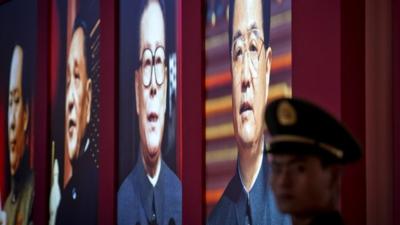 A Chinese paramilitary policeman stands guard next to a display showing four generations of Chinese leaders