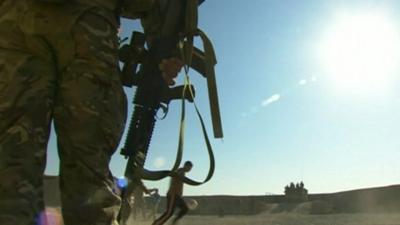 Armed Royal Marine watching soldiers playing football