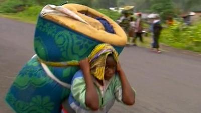 A civilian fleeing with belongings strapped to her back