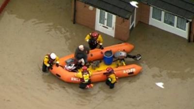 Aerial shot of man being rescued from his flooded house by dinghy