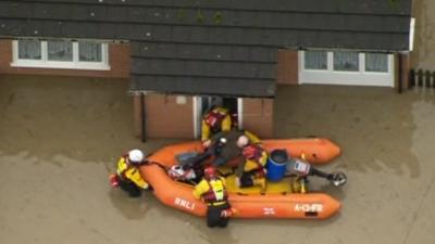 Rescue boat helping someone from their flooded house