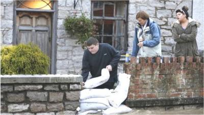 A man adds sandbags to a flood defence in an attempt to stop floodwaters entering a home in St Asaph, north Wales