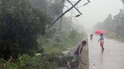 Residents brave heavy rains next to a tilted electric post after Typhoon Bophal hit the city of Tagum