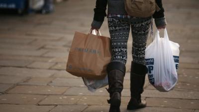 A woman carries several shopping bags from discount shops