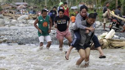 Residents cross a river in the flood-hit village of Andap